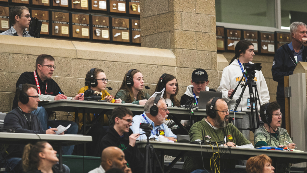 students broadcasting a game at a high school in the media row